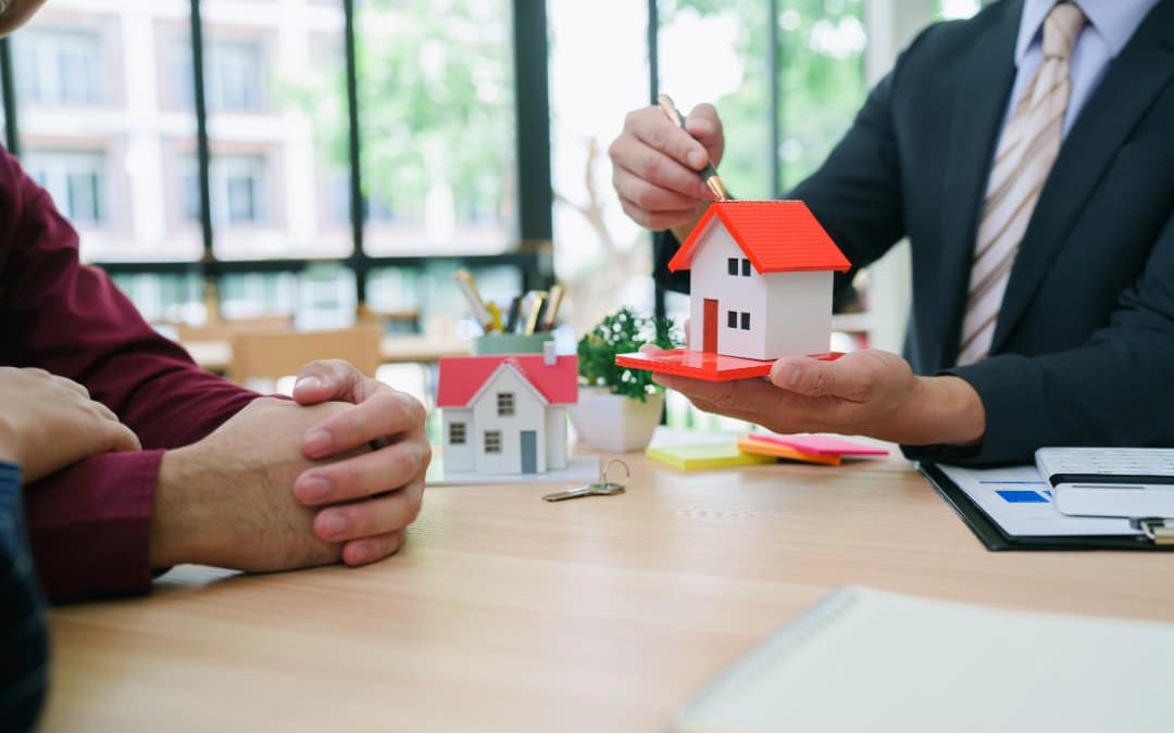 Couple consulting with a real estate agent in a cozy office, reviewing home-buying rules options with property listings on the table.