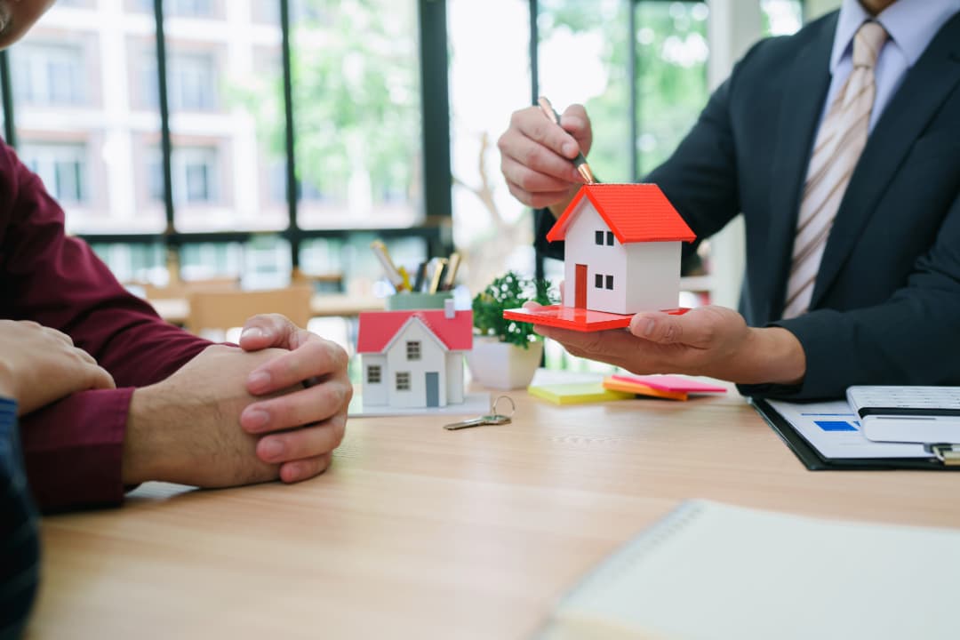 Couple consulting with a real estate agent in a cozy office, reviewing home-buying rules options with property listings on the table.